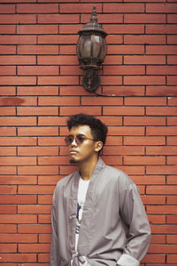 Portrait of young man standing against brick wall