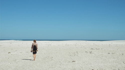 Rear view of woman walking on beach against clear blue sky