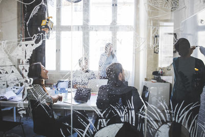 Creative business professionals looking at female colleague explaining strategy over whiteboard during meeting in office