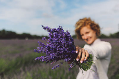Close-up of woman holding lavender flowers on field against sky