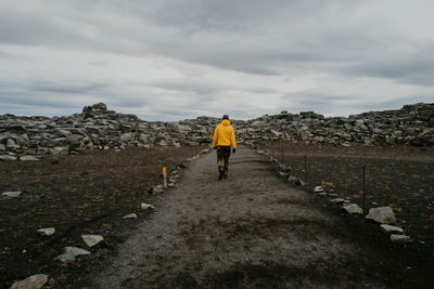 Man in yellow jacket walking on the road towards the rocks in iceland