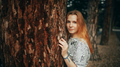 Young woman standing against tree trunk