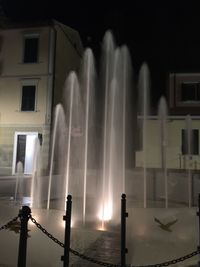 Water fountain on street against illuminated buildings at night