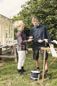 Woman showing phone to mature man while making shed at farm