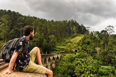 Man sitting on railway bridge against mountain