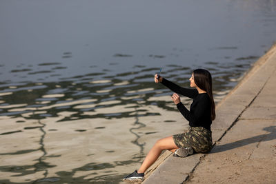 Cute young girl taking photos of herself with the lake in the background