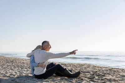 Man pointing at sea sitting with arm around woman on beach