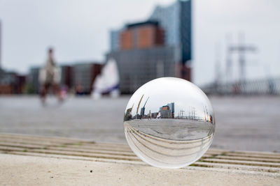 Close-up of crystal ball on glass against buildings in city