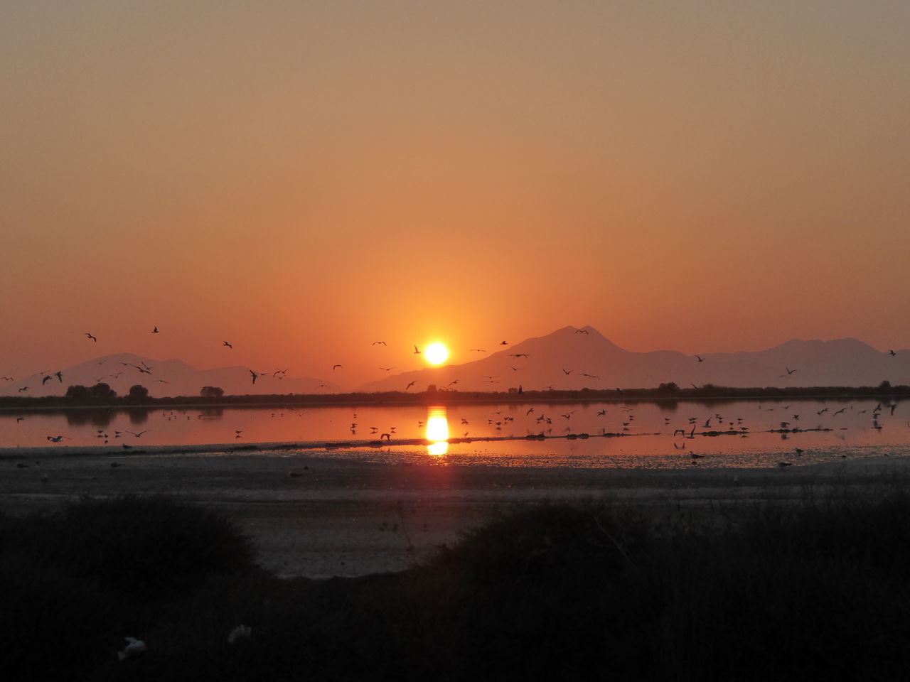 sunset, water, scenics, tranquil scene, tranquility, sun, orange color, lake, reflection, calm, beauty in nature, silhouette, idyllic, majestic, nature, vibrant color, standing water, non-urban scene, sky, vacations, no people, sea, back lit, remote, atmospheric mood, atmosphere