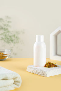 White bottle, calendula flowers and petals on a minimalistic sunny yellow background