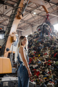 Portrait of young woman standing against garbage heap