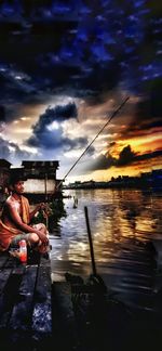 Man fishing in lake against sky during sunset