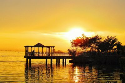 Silhouette gazebo by lake against sky during sunset