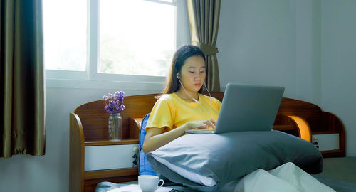 Woman using mobile phone while sitting on bed at home