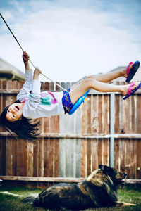 Side view of girl swinging over dog against sky