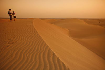 Man and woman on sand dune against sea at sunset