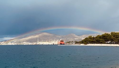 Scenic view of rainbow over sea and mountains against sky