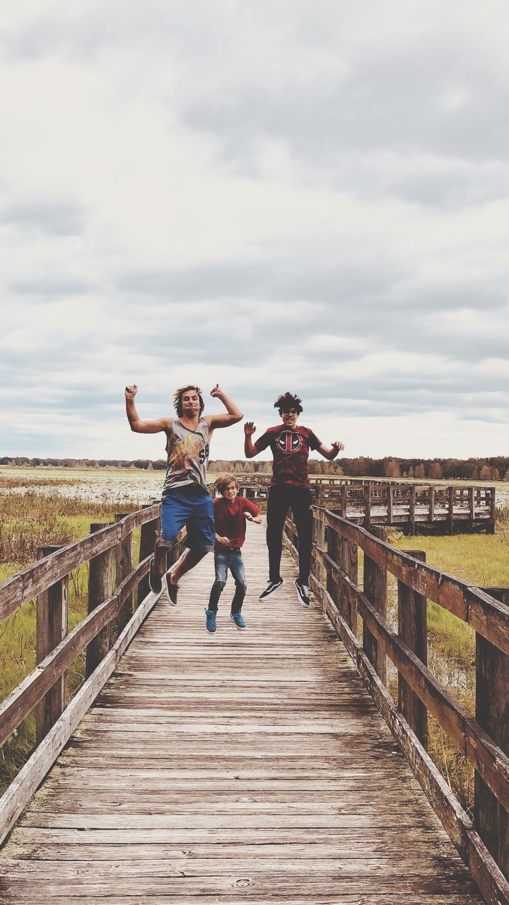 sky, full length, real people, leisure activity, lifestyles, nature, railing, cloud - sky, day, men, males, emotion, people, the way forward, direction, casual clothing, built structure, women, architecture, wood - material, human arm, positive emotion, outdoors, footbridge, arms raised