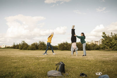 Teenage girl helping female friend to do handstand on grass in park