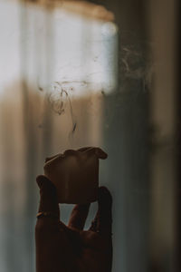 Cropped hand of woman holding candle against curtain