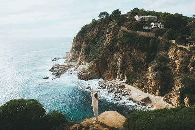 Rear view woman standing on cliff against sea 