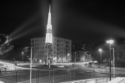 Illuminated buildings by street against sky at night