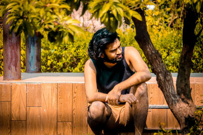 Young man sitting by plants against trees