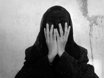 Cropped image of person hand covering face against wall