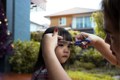 Mother cutting daughter hair against houses