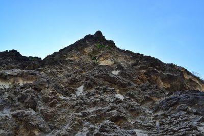 Low angle view of cliff on mountain against clear blue sky