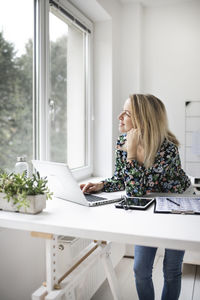 Smiling businesswoman looking out of window while sitting at office