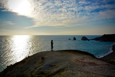Silhouette man standing on rock by sea against sky during sunset