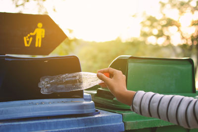 Cropped hand of woman putting plastic bottle in garbage can