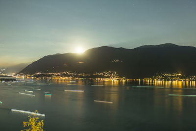 Illuminated city by sea against sky at night