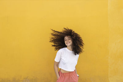 Carefree woman tossing hair in front of yellow wall