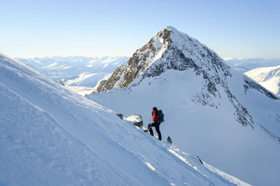 Woman hiking on snowcapped mountain against clear sky