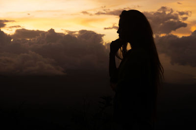 Side view of woman standing on mountain against sky during sunset