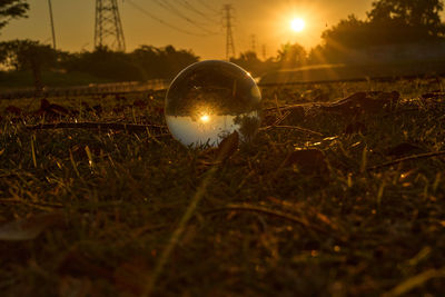 Close-up of crystal ball on field against sky during sunset