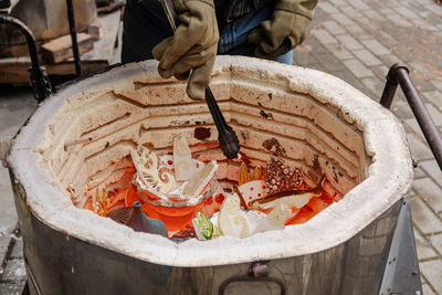 An artist wearing protective gloves loads ceramic raku ware in a red hot updraft furnace