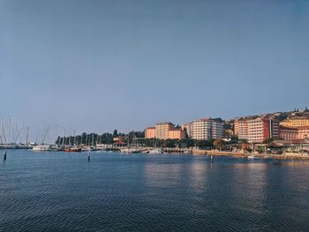 Sailboats in city by sea against clear sky