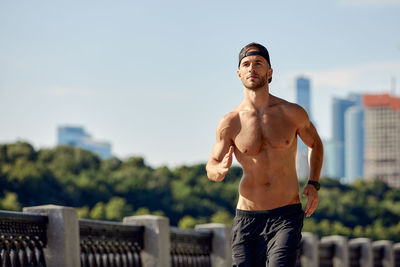 Portrait of shirtless man standing against sky