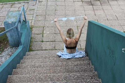 High angle view of woman holding bra while sitting on steps