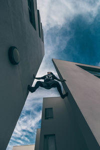Low angle view of man climbing on wall against sky in city