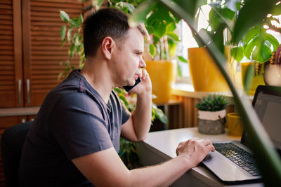 Side view of young man using mobile phone while sitting at home