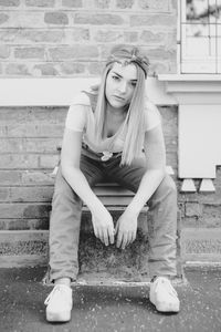Portrait of young woman sitting against wall