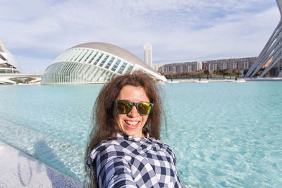 Portrait of smiling young woman wearing sunglasses against sky