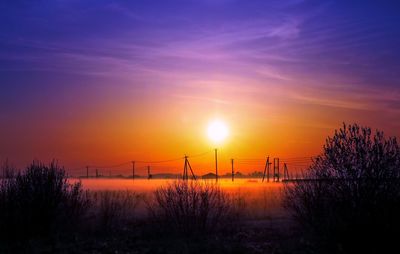 Silhouette trees and electricity pylon against romantic sky at sunset