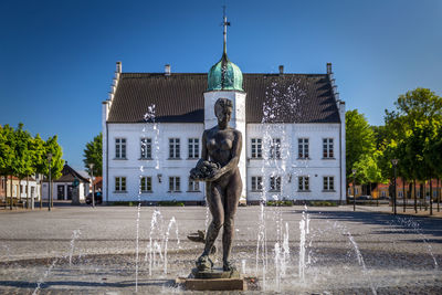 Statue by fountain against buildings in city against sky