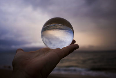 Cropped hand holding crystal ball on beach