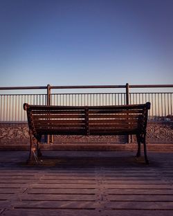 Empty bench by railing against clear blue sky